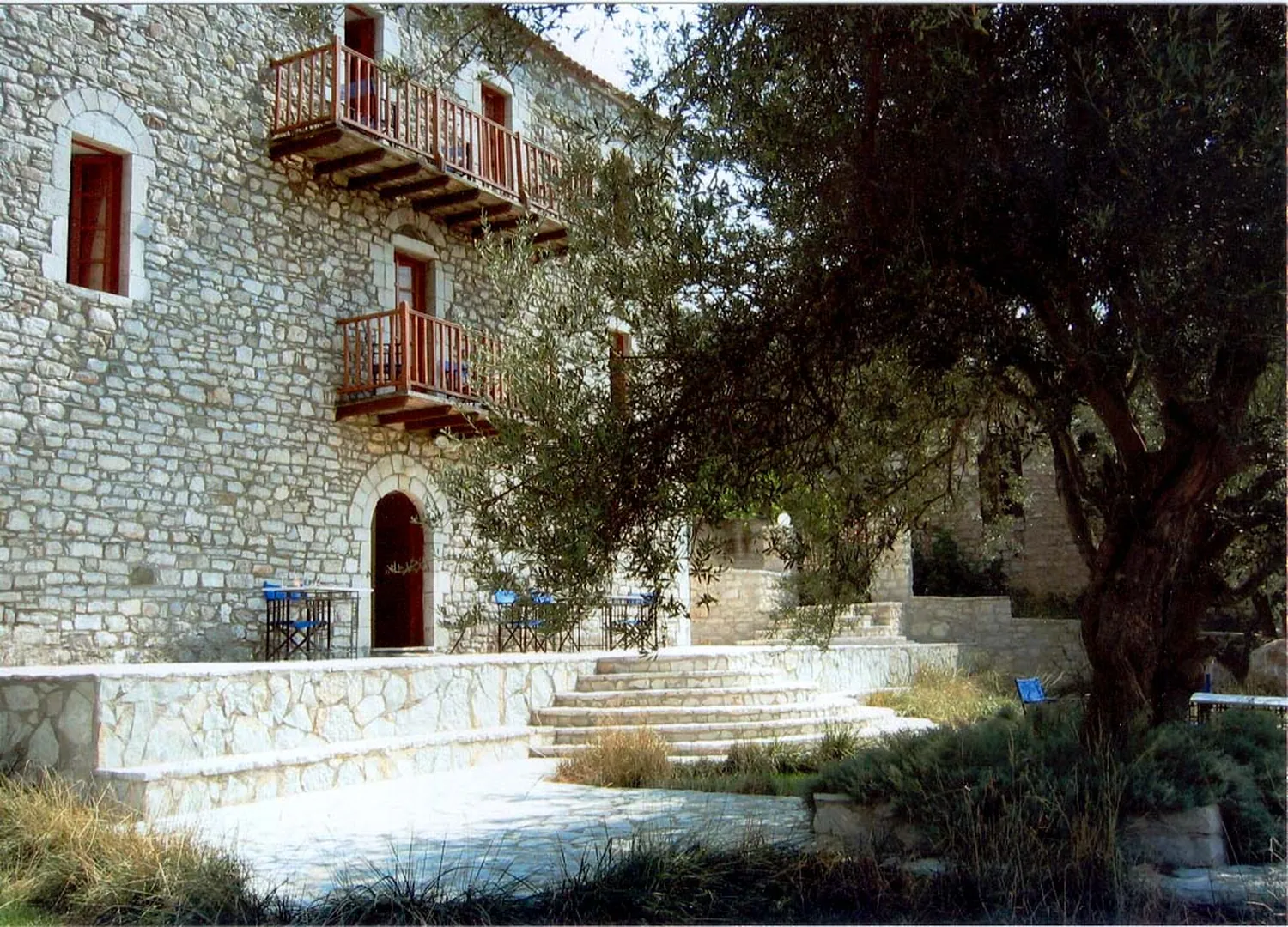 Η πέτρινη πρόσοψη με τα ξύλινα μπαλκόνια και τη μεγάλη ελιά